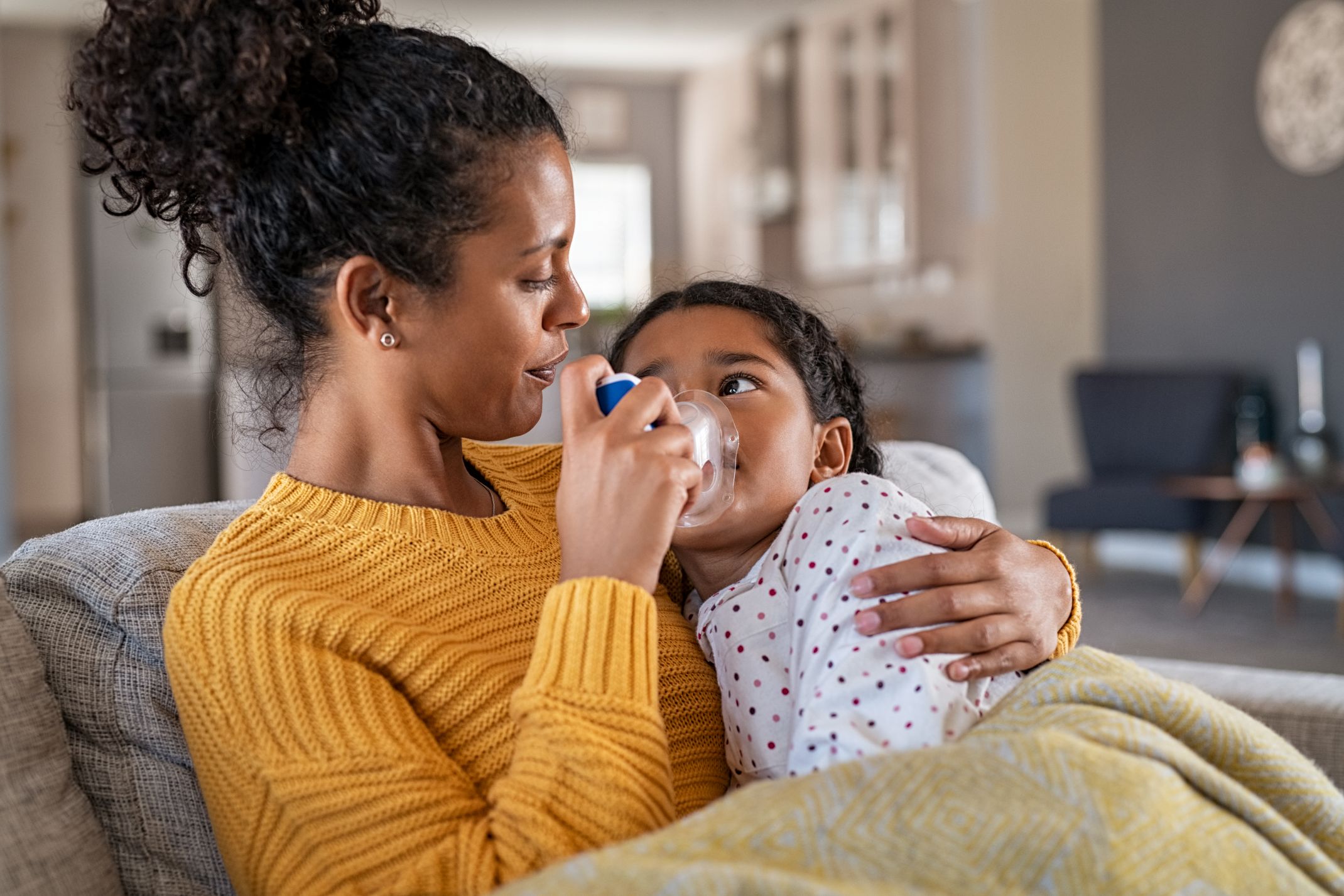 Mother assisting daughter with nebulizer asthma treatment at home in fall