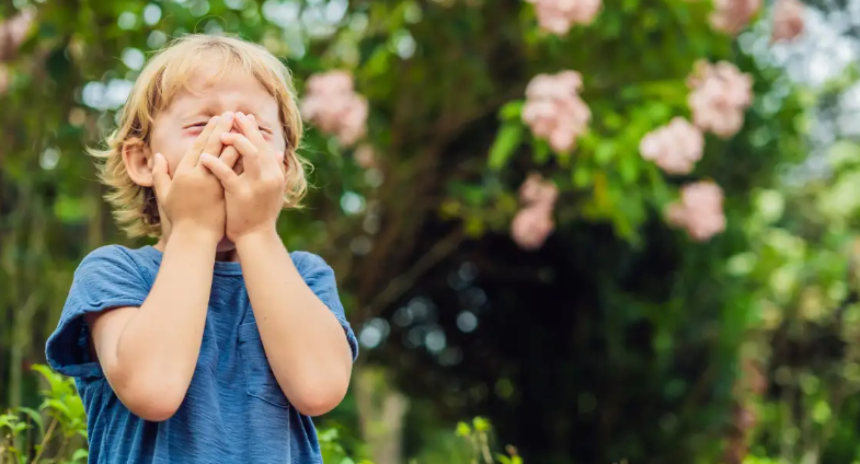 Young child outdoors in spring holding hands over face while experiencing seasonal allergy symptoms