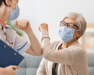 A physician and patient wearing masks and touching elbows instead of shaking hands