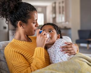 Mother assisting daughter with nebulizer asthma treatment at home in fall