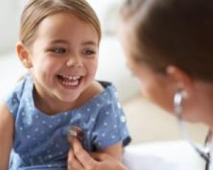 Smiling girl having a wellness check with doctor using stethoscope in pediatric office