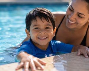 Hispanic mother supervising her young son in a swimming pool while practicing water safety during summer.