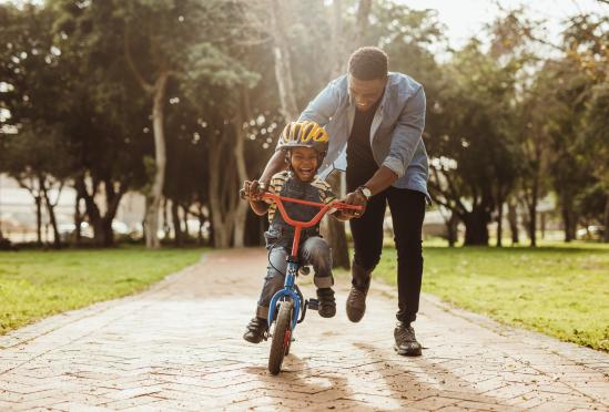 A father helping his child ride a bike in a park