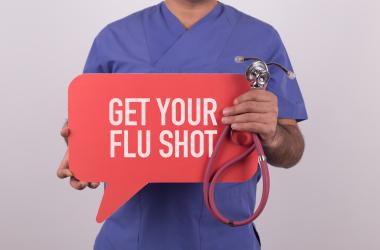 A physician holding a flu shot sign