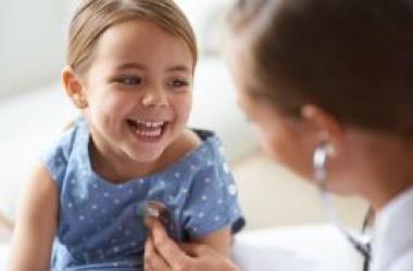 Smiling girl having a wellness check with doctor using stethoscope in pediatric office