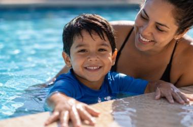 Hispanic mother supervising her young son in a swimming pool while practicing water safety during summer.