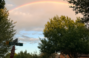Rainbow in a cloudy sky above a neighborhood.