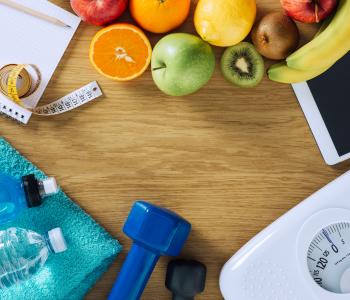 Fitness and weight loss concept, dumbbells, white scale, towels, fruit, tape measure and digital tablet on a wooden table, top view