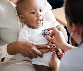 A mother holding her child while a physician listens to their breathing