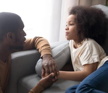 A father hold daughter hand looking at child lying on sofa