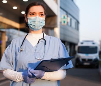 A physician with a clipboard standing in front of the facility